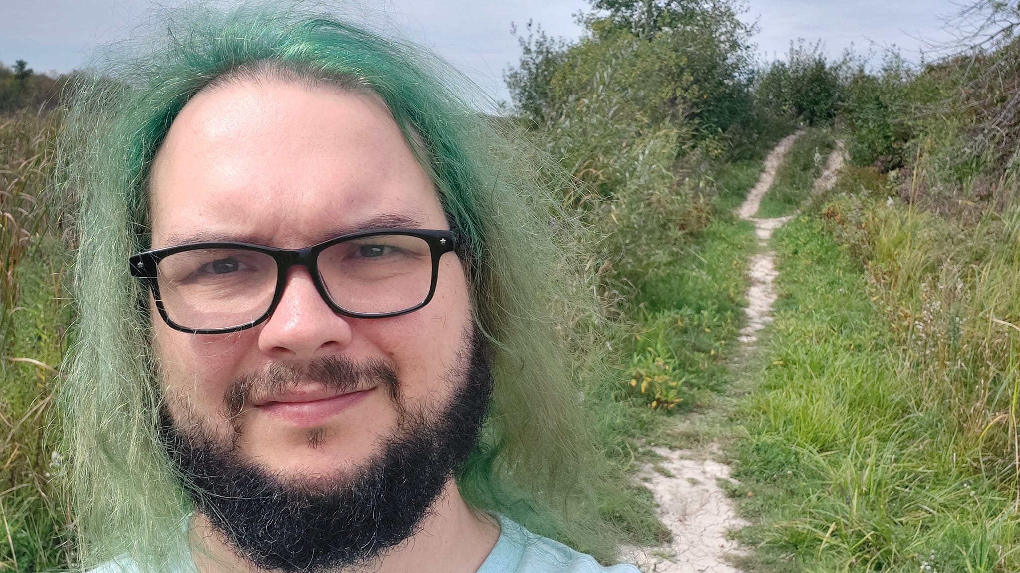 A man with green hair stands in front of a small hill, Photo 1